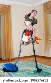 Smiling Female Vacuuming Carpet Floor At Home In Living Room Jumping Up On Brush, Young Lady In Apron Cleaning Apartment With Blue Vacuum Cleaner