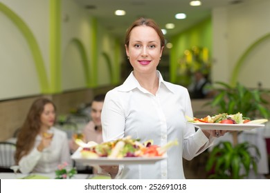 Smiling Female Waiter Serving Guests Table In Restaurant