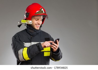 Smiling Fireman Using Smart Phone. Waist Up Studio Shot Isolated On White.