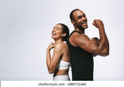Smiling fitness couple standing back to back against white background. Fit couple showing arm muscles standing together.