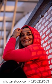 Smiling fitness girl. She is sitting on the bridge, wears a hood on her head 