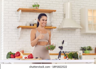 Smiling fitness vlogger filming culinary video blog about healthy food. Happy positive fit woman blogger recording vlog on mobile phone, giving dieting and cooking advice, sharing vegan salad recipe - Powered by Shutterstock