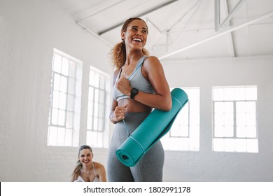 Smiling fitness woman standing in a fitness studio carrying a yoga mat. Portrait of a young woman at a fitness training centre. - Shutterstock ID 1802991178
