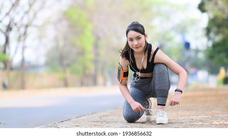 Smiling fitness woman tie shoelaces  getting ready for jogging outdoors.