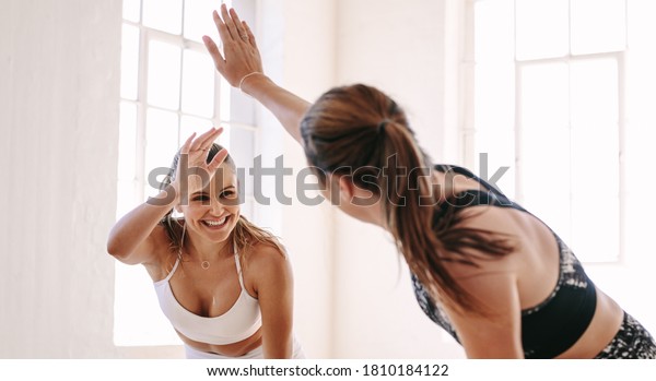 Smiling fitness women raise hands to give a high\
five during workout. Cheerful athletic women enjoying fitness\
training at a fitness\
studio.