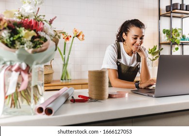 Smiling Flower Shop Owner Using Laptop Computer. Female Florist Working On Laptop At Counter.