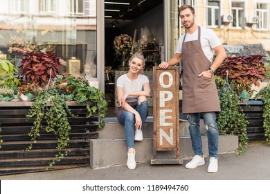 smiling flower shop owners looking at camera on street with open signboard - Powered by Shutterstock