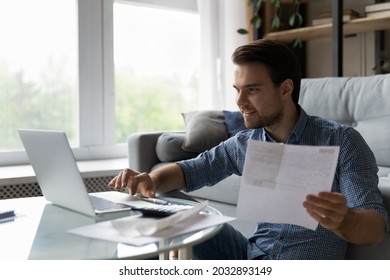 Smiling focused millennial man satisfied with income, savings calculating taxes, budget, costs, paying bill, insurance, mortgage fee, checking paper invoice, doing accounting work on laptop at home