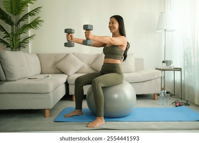 Sonriente y concentrada, una mujer combina el entrenamiento de fuerza y estabilidad central con pesas y una pelota de ejercicios, enfatizando la conveniencia de mantenerse en forma en casa.