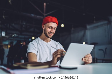 Smiling Focused Young Guy Sitting At Table And Drawing On Big Tablet With Stylus Pen While Working With Inspiration In Modern Garage Office 