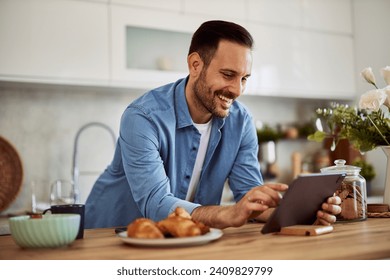 A smiling freelance man responds to a video call from a client on a tablet while leaning on a kitchen counter. - Powered by Shutterstock