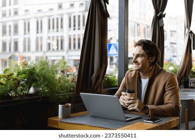 Smiling freelancer in coat holding coffee to go near laptop and smartphone in cafe	 - Powered by Shutterstock