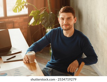 Smiling Freelancer Guy At Laptop Holding Coffee Cup Looking At Camera Sitting At Workdesk In Modern Office. Selective Focus - Powered by Shutterstock