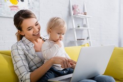 Smiling Freelancer Pointing At Laptop While Holding Little Son