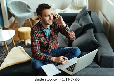 Smiling Freelancer Talking On Mobile Phone While Working On A Computer In The Living Room. 