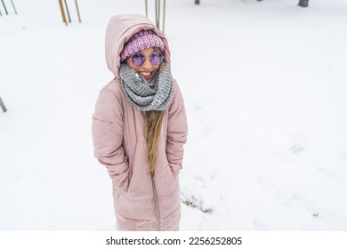 Smiling freezing woman with hands in winter coat pockets and sunglasses on standing in the snow. High quality photo - Shutterstock ID 2256252805