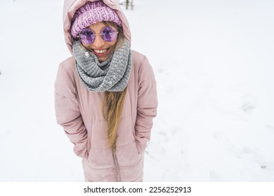 Smiling freezing woman with hands in winter jacket pockets standing in the snow. High quality photo - Shutterstock ID 2256252913