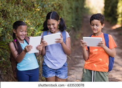 Smiling friend using digital tablets while walking at natural parkland