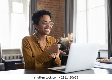 Smiling friendly African American therapist in glasses talking on video call, using sign language, speaking to patient with hearing disability, deafness, showing gestures at screen