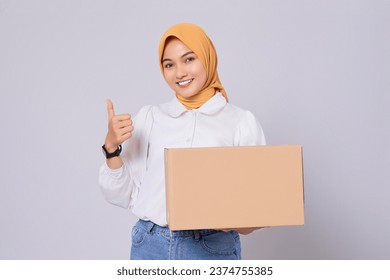 Smiling friendly Asian Muslim Woman in white shirt holding package box and showing thumbs up or like isolated on white background. Shopping and delivery concept - Powered by Shutterstock