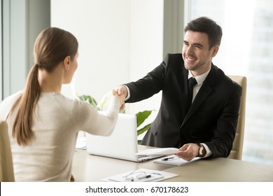 Smiling friendly businessman shaking hands with woman sitting at office desk, holding agreed negotiation document, congratulating female partner with successful deal, handshaking new team member, HR  - Powered by Shutterstock