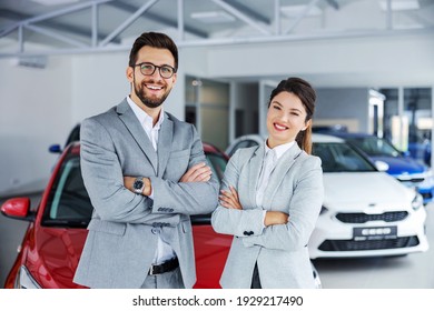 Smiling, friendly car sellers standing in car salon with arms crossed and announcing retail.