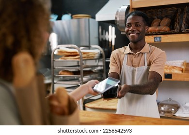 Smiling friendly cashier desk worker accepting contactless payment - Powered by Shutterstock