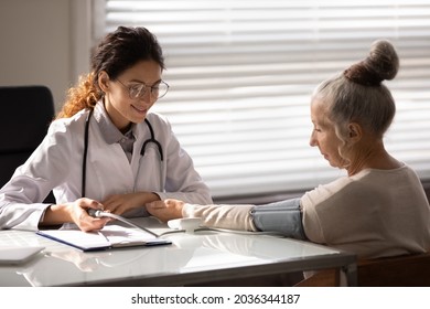 Smiling Friendly Doctor Checking Blood Pressure Of Older Female Patient At Appointment In Office, Using Sphygmomanometer, Examining Woman With Hypertension Or Hypotension, Fast Heartbeat