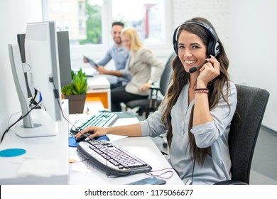 Smiling friendly female call-center agent with headset working on support hotline in the office - Shutterstock ID 1175066677