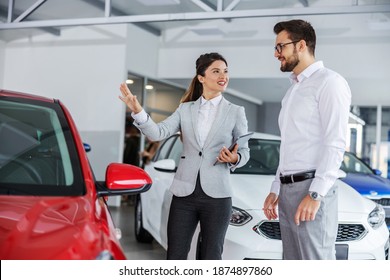 Smiling friendly female car seller with tablet in hands talking about car specifications to a man who wants to buy a car. Car salon interior. - Powered by Shutterstock