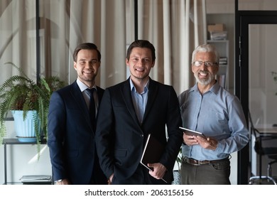 Smiling friendly group of three businessmen of different age private company staff posing for office portrait. Young male team leader ceo and two men aged and millennial subordinates looking at camera