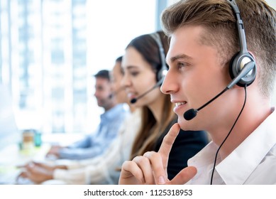 Smiling friendly man working in call center office with team as telemarketing customer service agents
