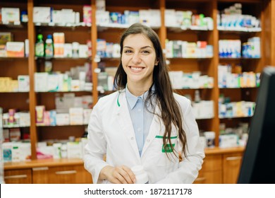 Smiling friendly pharmacist at the counter working in a pharmacy store. Pharmaceutical professional recommending an over the counter supplement. Giving advice about medication.Happy health care worker