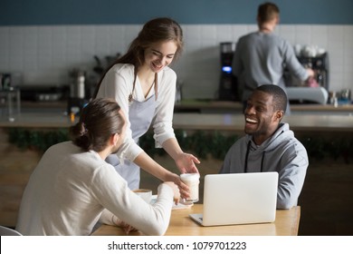 Smiling friendly waitress serving coffee drinks to diverse male friends meeting at cafe table, cafeteria server and multiracial visitors laughing together at funny joke in modern coffee shop house