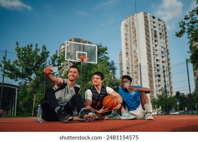 Smiling friends capture a selfie memory on a sunny basketball court with urban buildings behind, blending technology, sport, and friendship - Powered by Shutterstock