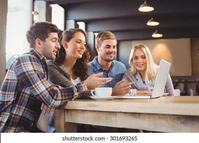 Smiling Friends Drinking Coffee And Pointing On Laptop Screen At Coffee Shop