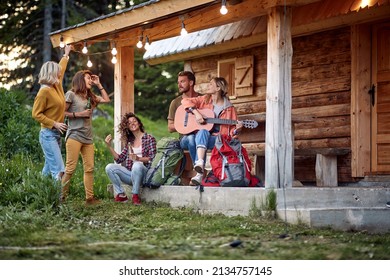 Smiling friends drinking and playing guitar in front of wooden cottage on the terrace. - Powered by Shutterstock