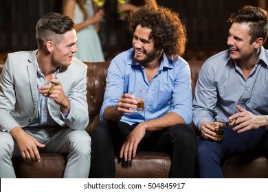 Smiling friends interacting with each other while having cigar and whisky in bar - Powered by Shutterstock