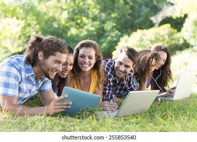 Smiling friends in the park using tablet pc and laptop on a sunny day - Powered by Shutterstock