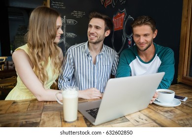 Smiling friends using laptop while sitting at table in cafe