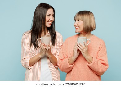 Smiling fun elder parent mom with young adult daughter two women together wear casual clothes hold in hand cup of coffee look to each other isolated on plain blue cyan background. Family day concept - Powered by Shutterstock