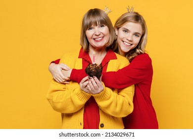Smiling fun woman 50s in red shirt crown with teenager girl 12-13 year old Grandmother granddaughter hold birthday cake blow out candle hug isolated on plain yellow background Family lifestyle concept