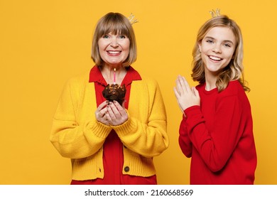 Smiling Fun Woman 50s In Red Shirt Crown With Teenager Girl 12-13 Years Old. Grandmother Granddaughter Hold Birthday Cake Blow Out Candle Isolated On Plain Yellow Background Family Lifestyle Concept