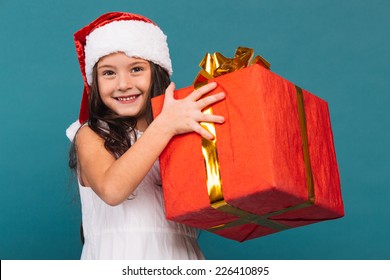 Smiling Funny Child (kid, Girl) In Santa Red Hat Holding Christmas Gift In Hand. Christmas Concept.