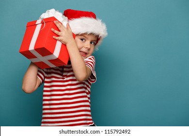 Smiling  Funny Child In Santa Red Hat Holding Christmas Gift In Hand. Christmas Concept.