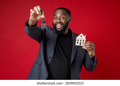 Smiling funny young african american business man 20s wearing classic jacket suit standing hold house bunch of apartment keys looking camera isolated on bright red color background studio portrait