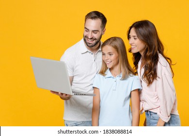 Smiling Funny Young Parents Mom Dad With Child Kid Daughter Teen Girl In Basic T-shirts Using Laptop Pc Computer Isolated On Yellow Background Studio Portrait. Family Day Parenthood Childhood Concept