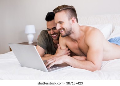 Smiling Gay Couple Using Laptop On Bed