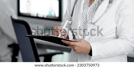 Smiling general practitioner taking notes in medical history of patient, writing down symptoms, complaints and anamnesis