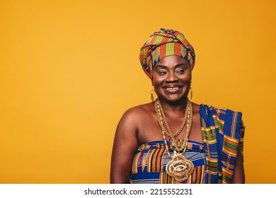 Smiling Ghanaian woman wearing a traditional attire against a yellow background. Happy black woman dressed in colourful Kente cloth and golden jewellery. Mature elegant woman embracing her rich cultur - Powered by Shutterstock